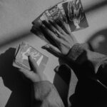 A dramatic black and white photo of hands holding tarot cards, casting shadows.